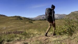 Backpacker hiking along Four Pass Loop in Colorado with grassy meadow in the background.