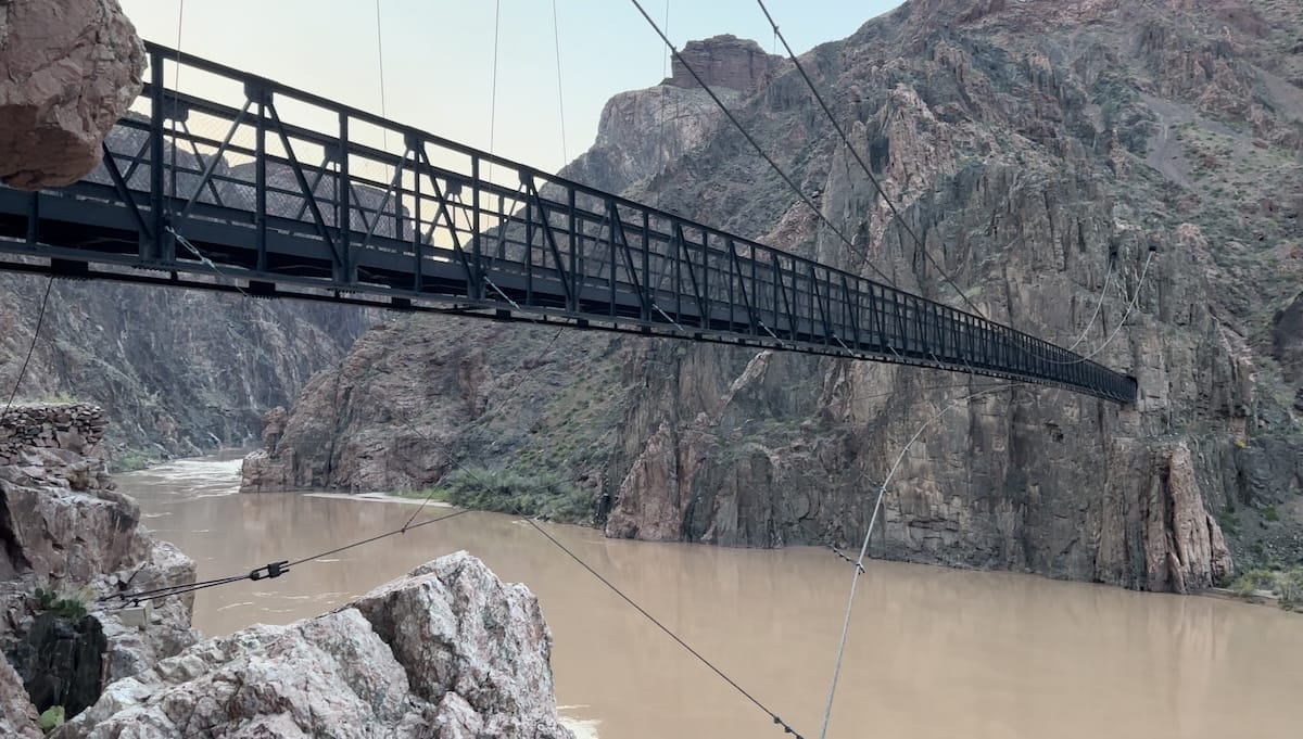 Black suspension bridge crossing the Colorado River in the Grand Canyon.