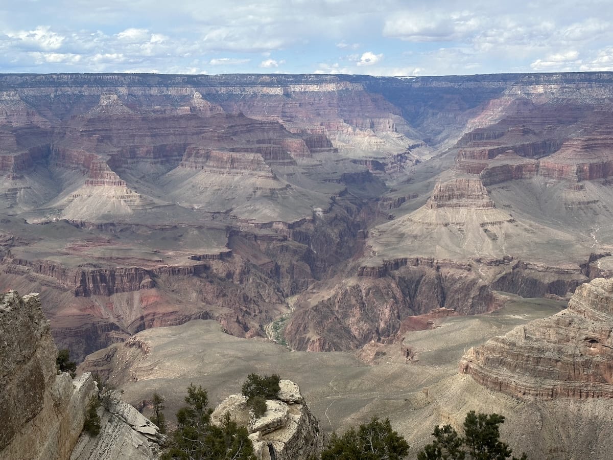 Panoramic view of the Grand Canyon with layered rock formations and a partly cloudy sky.