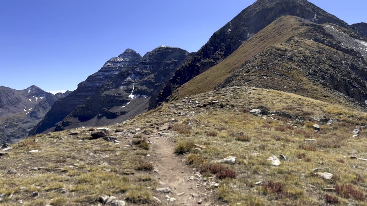 Mountain ridge trail with peaks under clear blue sky.