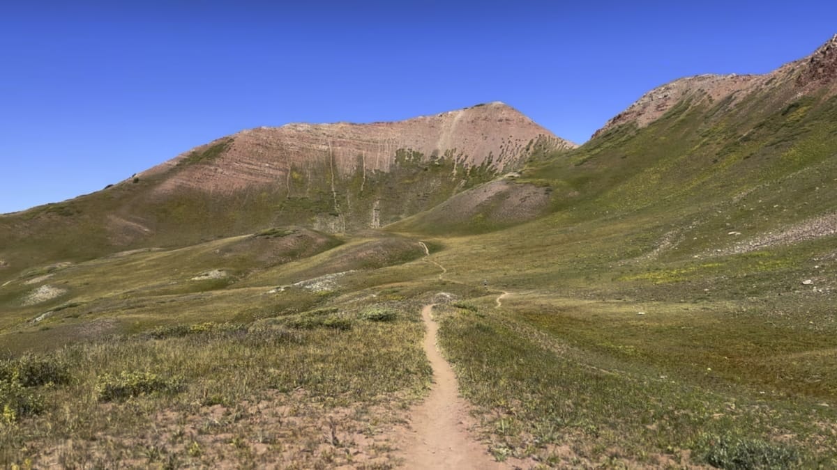 Mountain trail through open valley with red rock peak.