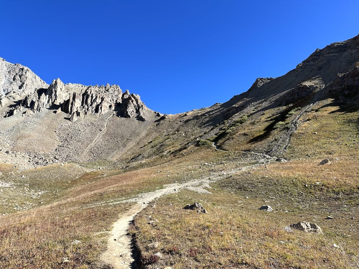 Approaching Trail Ryder Pass in an open valley under clear blue sky.