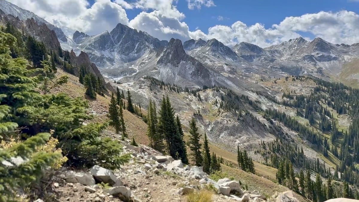 Rugged mountain peaks with evergreen forest along a hiking trail.