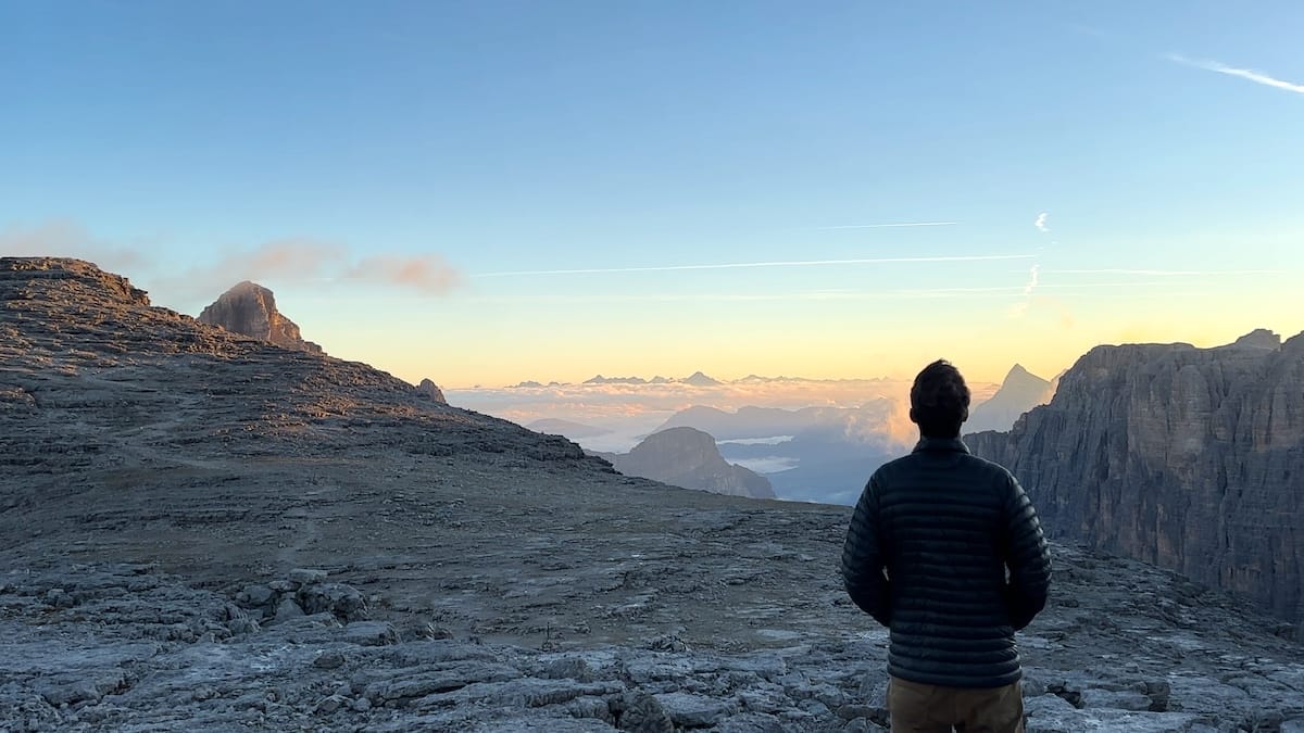 Hiker enjoying the sunrise on the Alta Via 2 wearing a black Ghost Whisperer down jacket.