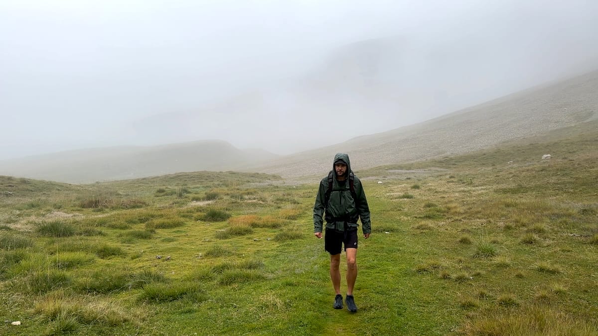 Alta Via 2 hiker in a green grassy meadow surrounded by fog and dampness.