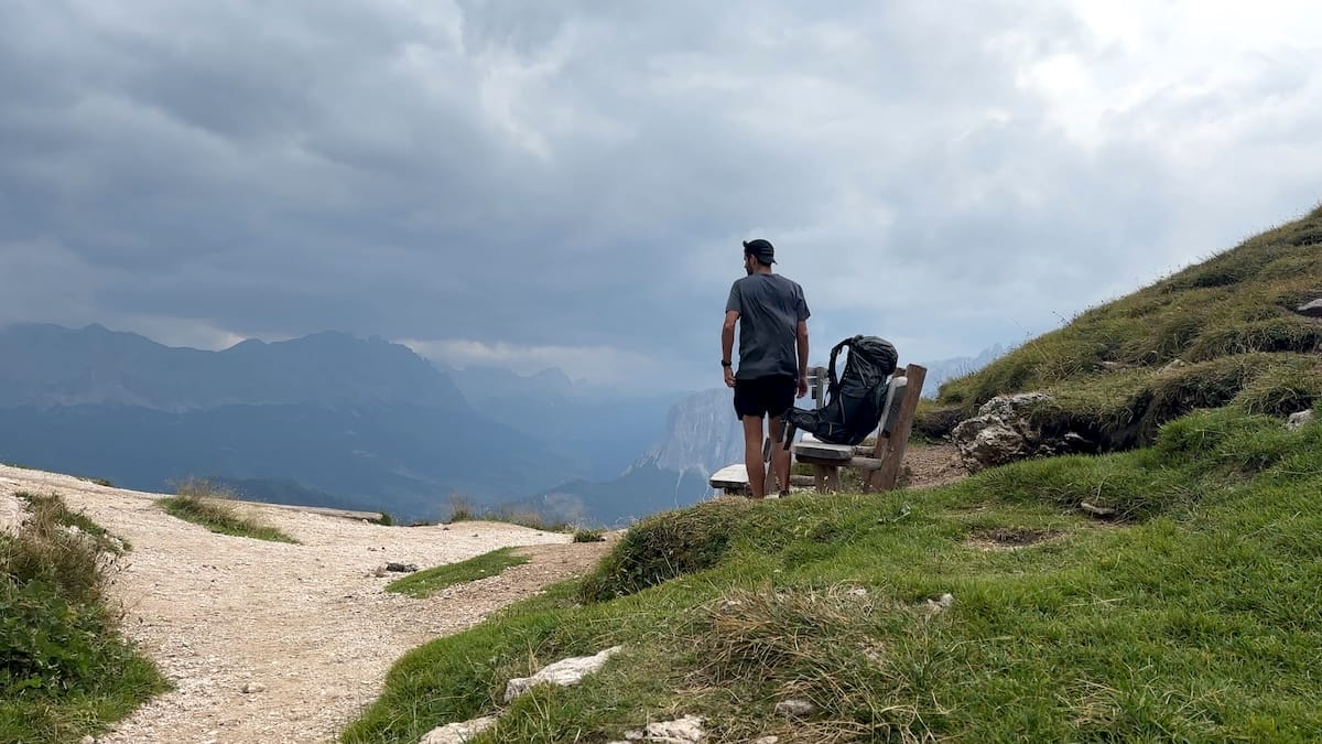 Hiker stopping for a break at a bench on the Forcella di Putia while hiking the Alta Via 2 in September with storm clouds in the distance.