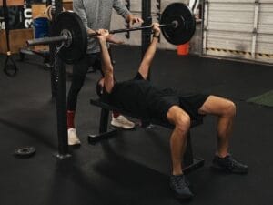 weightlifting-bench-press-workout Man lifting barbell during a bench press exercise, with trainer spotting.