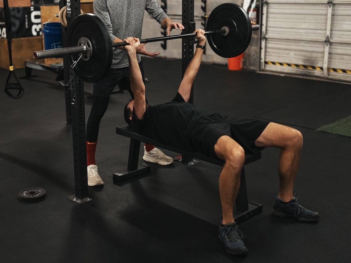 weightlifting-bench-press-workout Man lifting barbell during a bench press exercise, with trainer spotting.